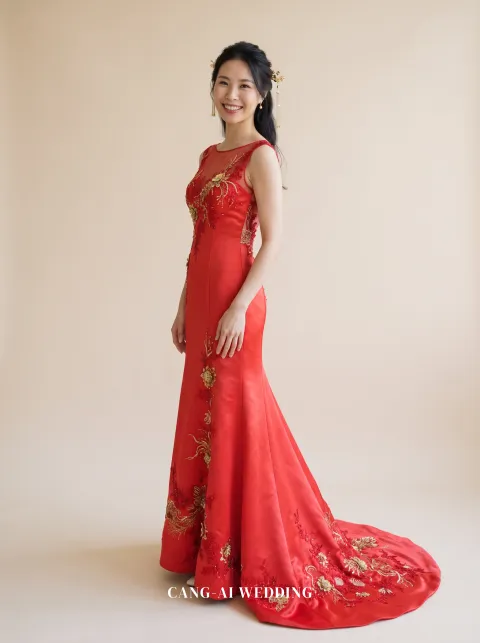 Front full-length of Jinhua, a red satin mermaid kua with a sheer neckline and raised gold flowers, turning back to the camera with a smile, reference 14-NR20.
