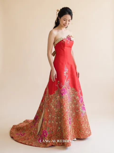 Front full-length of Fuyun, a red A-line with a gold sash across one shoulder, looking down at the skirt, reference 2-NR06.